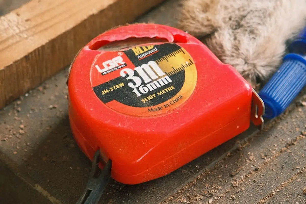 Red retractable tape measure on a dusty wooden workbench