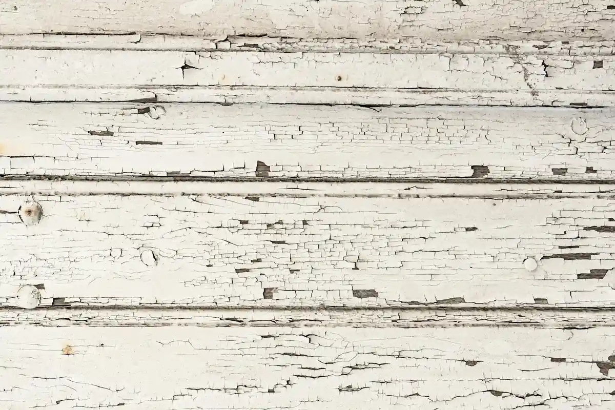 Close-up of weathered wooden boards with white peeling paint and visible cracks