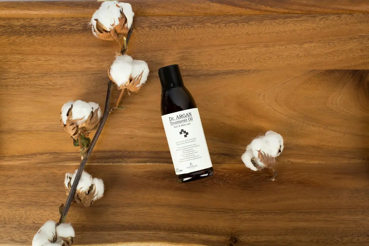 A dark bottle of oil placed on a wooden surface with white cotton stems nearby.