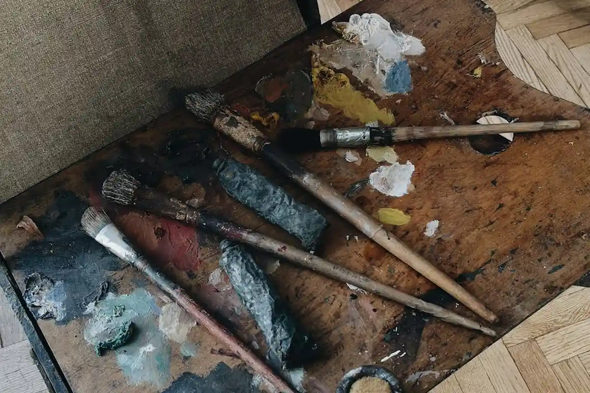 Assorted brushes and tools stained with oil on a wooden workbench, illustrating preparation steps for applying penetrating wood oils and oil-based finishes.