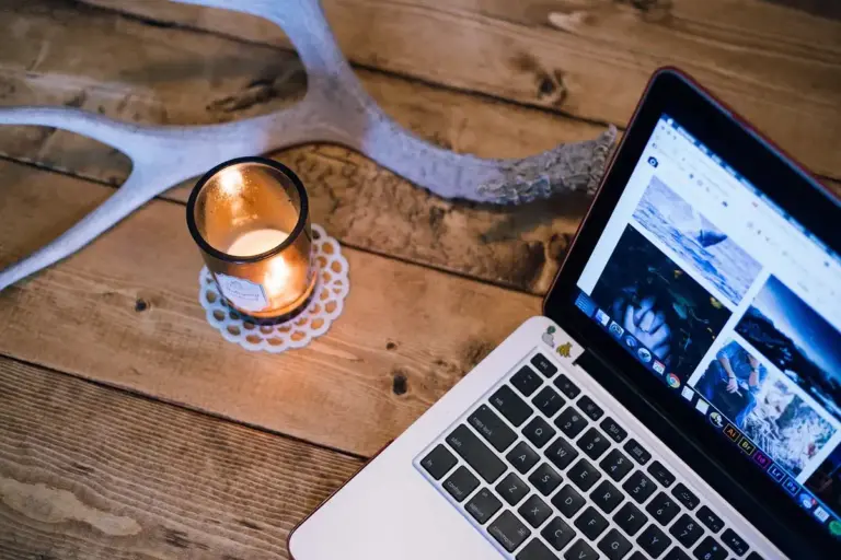 Wood table with a lit candle and a laptop, rustic decor with antler in background.