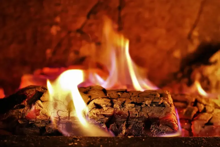 Close-up of glowing embers and small flames in a wood-burning fireplace