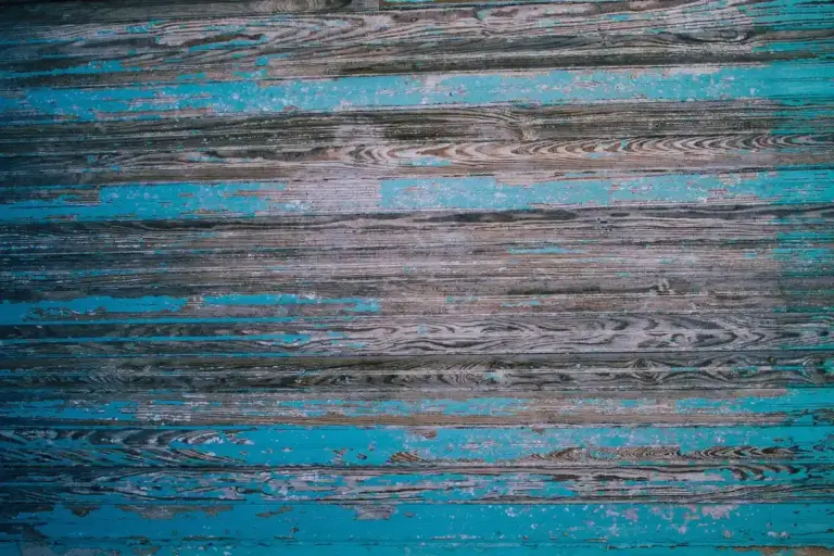Close-up of a wooden surface with turquoise blue paint peeling away to reveal the grain