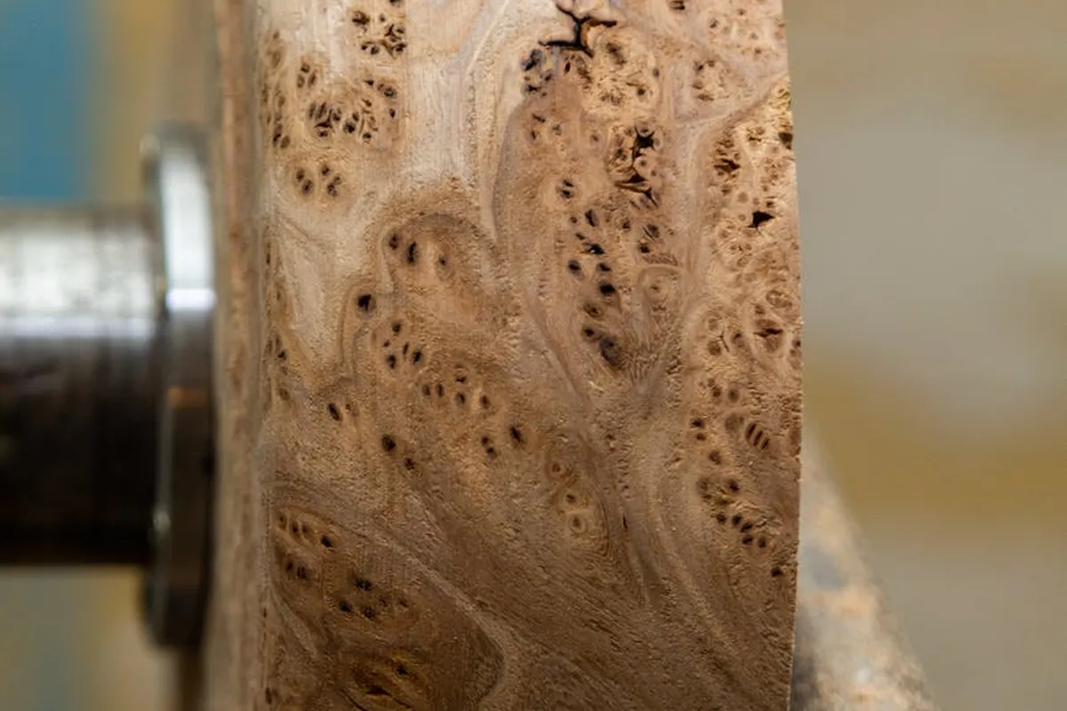 Close-up of a turning blank with rich natural figure and numerous small holes/pores on the surface, mounted near a lathe.