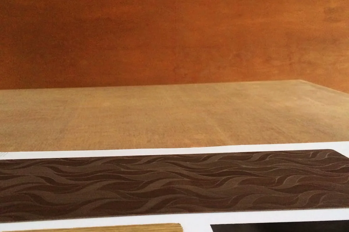 Decorative wood veneer sample with dark brown wavy grain pattern on a white surface.