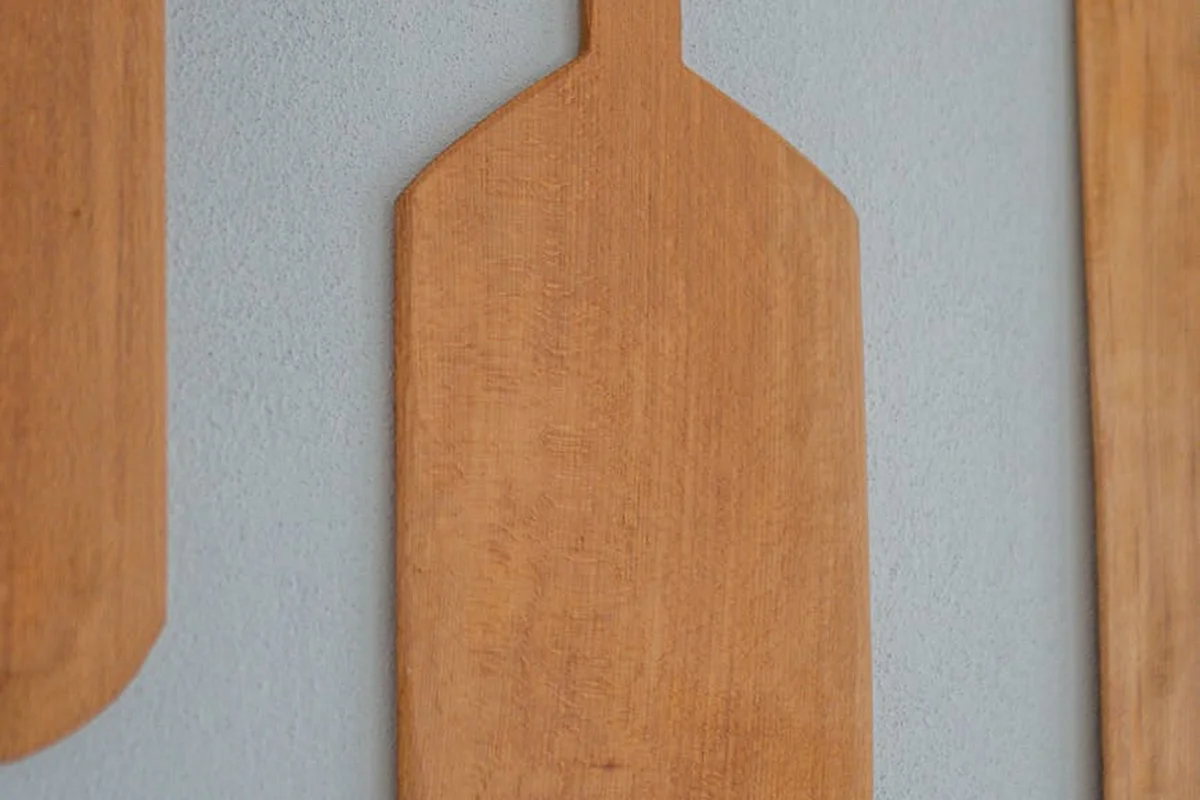Three wooden cutting boards with natural finishes hanging on a light gray wall.