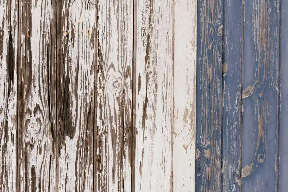 Two-tone weathered wooden boards, left with brown and white peeling paint and right with blue paint, showing exposed grain ready for refinishing.