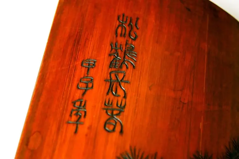 Close-up of a warm-toned wooden panel with vertical carved Chinese characters.
