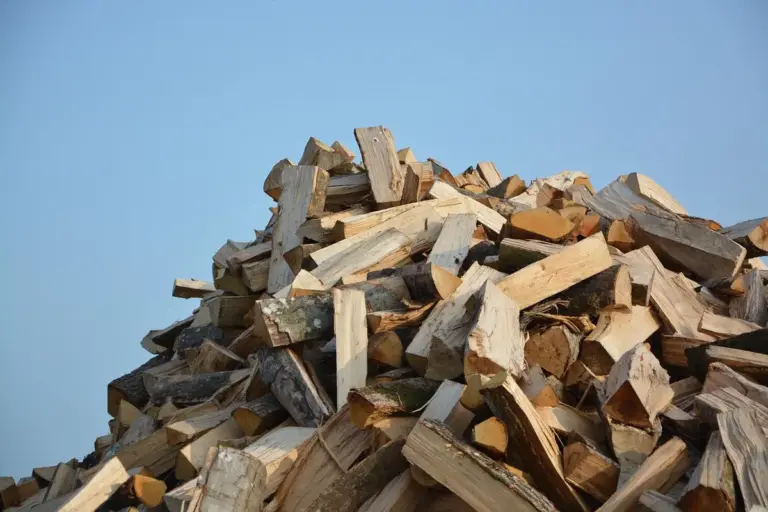 A large pile of split firewood stacked outdoors against a clear blue sky.