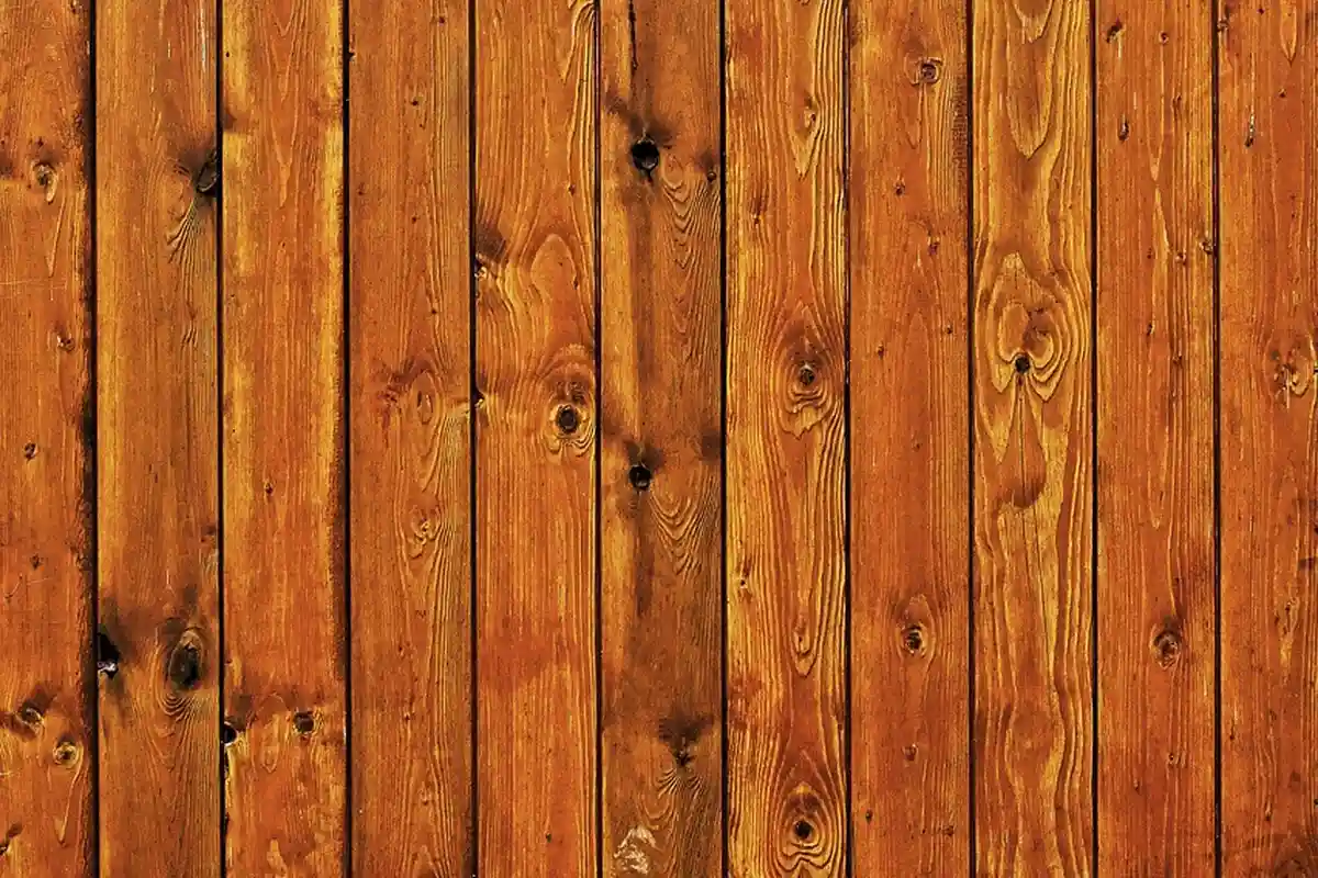 Vertical wooden fence planks with warm brown tones, displaying grain patterns and knots.