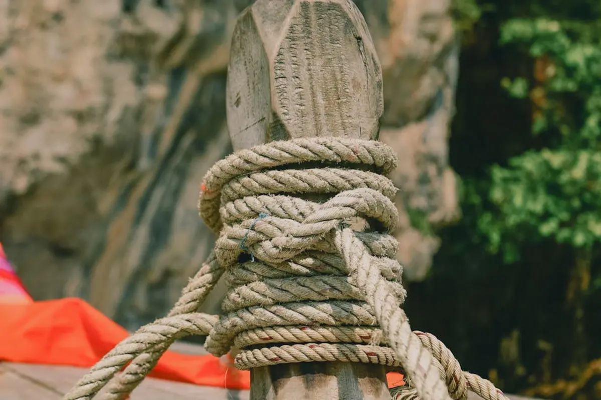 Close-up of a thick rope wrapped around a weathered wooden post outdoors, with blurred greenery in the background