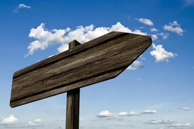 Blank wooden signboard on a post against a blue sky with scattered clouds