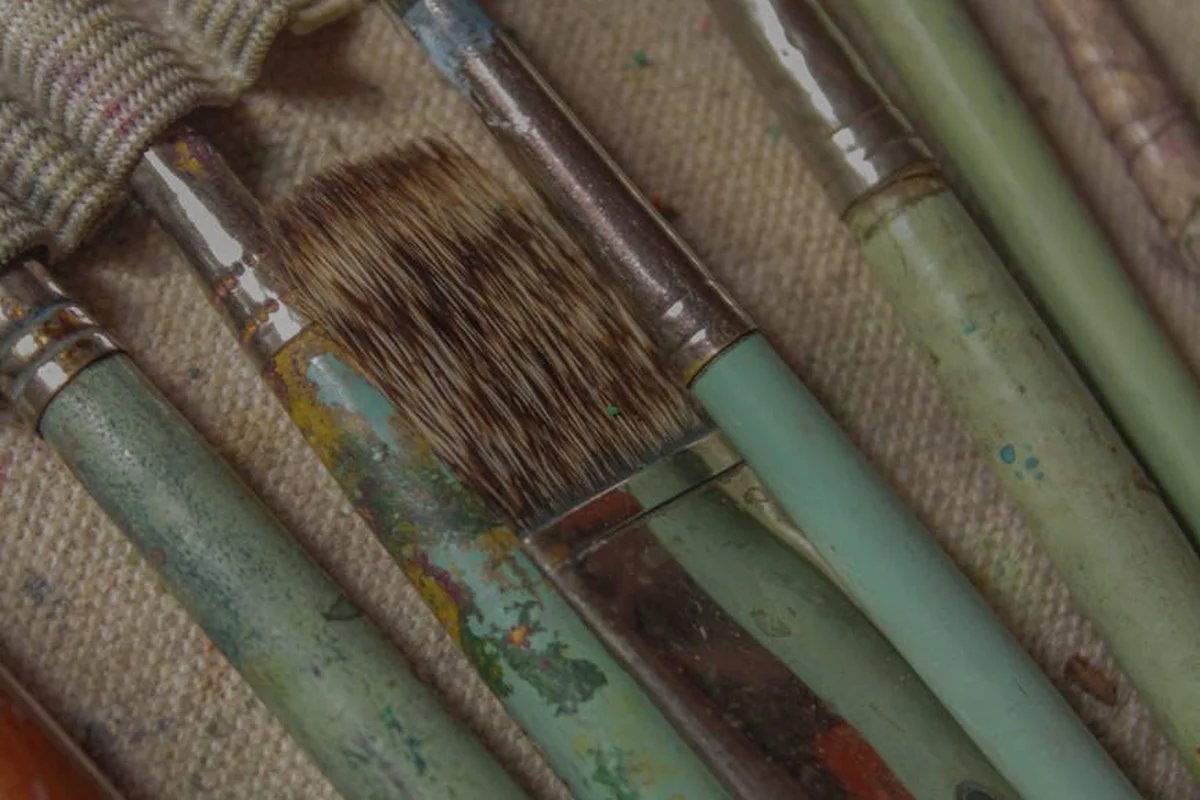 Close-up of weathered wood-staining brushes with green handles on a burlap background, illustrating eco-friendly staining practices.