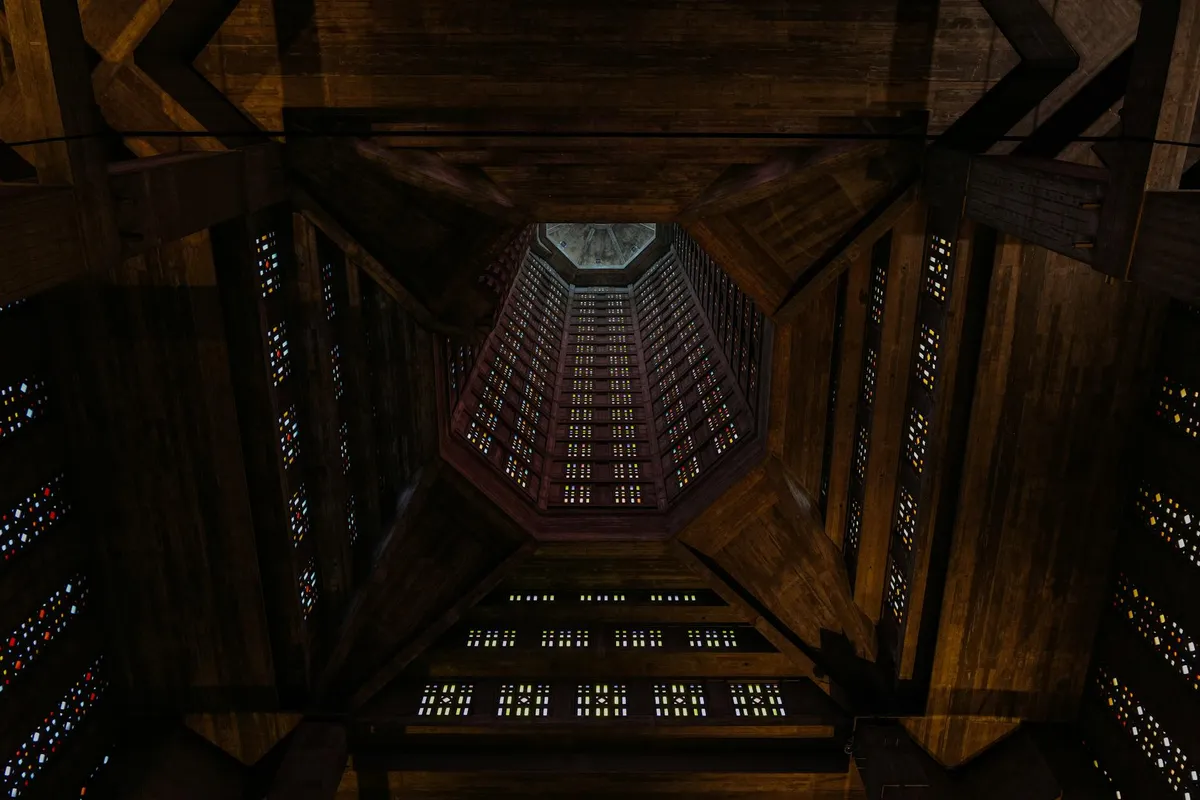 Interior view of a dark-stained wooden ceiling with exposed beams and small windows, seen from below.