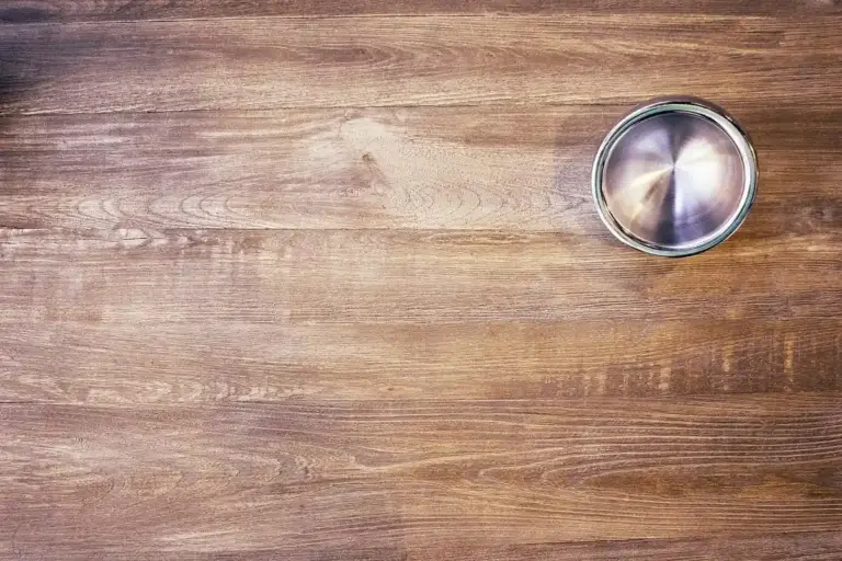 A close-up of a warm-toned wooden tabletop with a small metal lid in the upper-right corner.