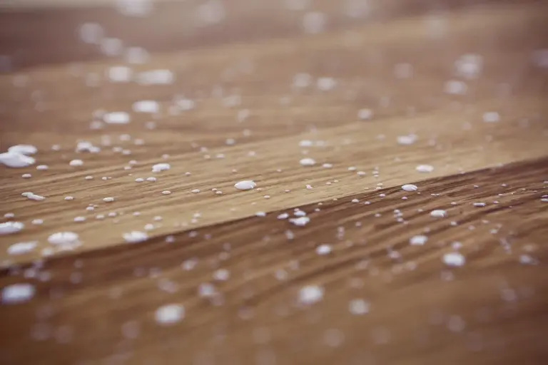Close-up of a wooden surface with scattered white specks, symbolizing protein-based interactions in hide glue.