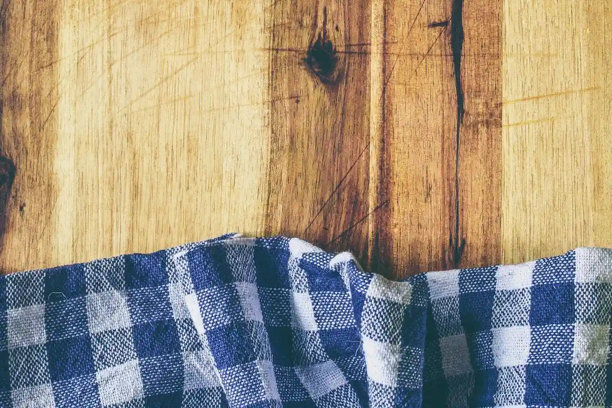 Close-up of a wooden tabletop with visible grain and a blue-and-white checkered cloth draped along the bottom edge.