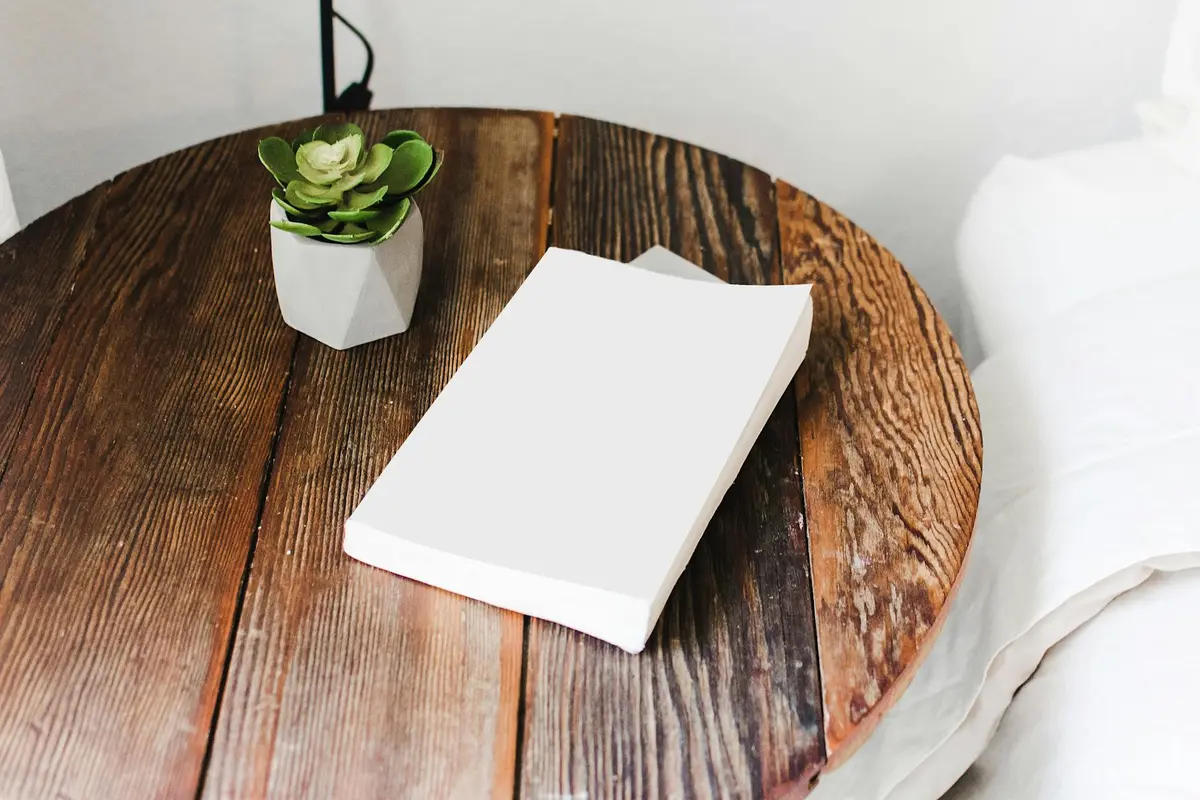 Round wooden table with a white notebook and a small succulent plant in a white geometric pot.