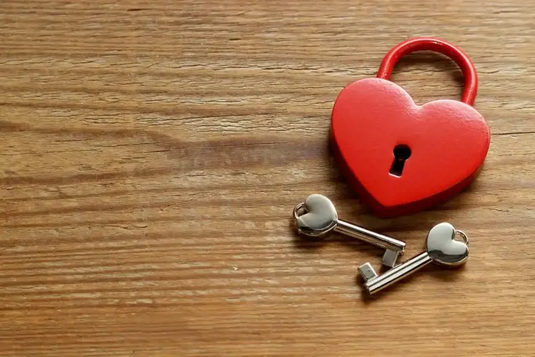 Red heart-shaped padlock with two metal keys on a wooden surface