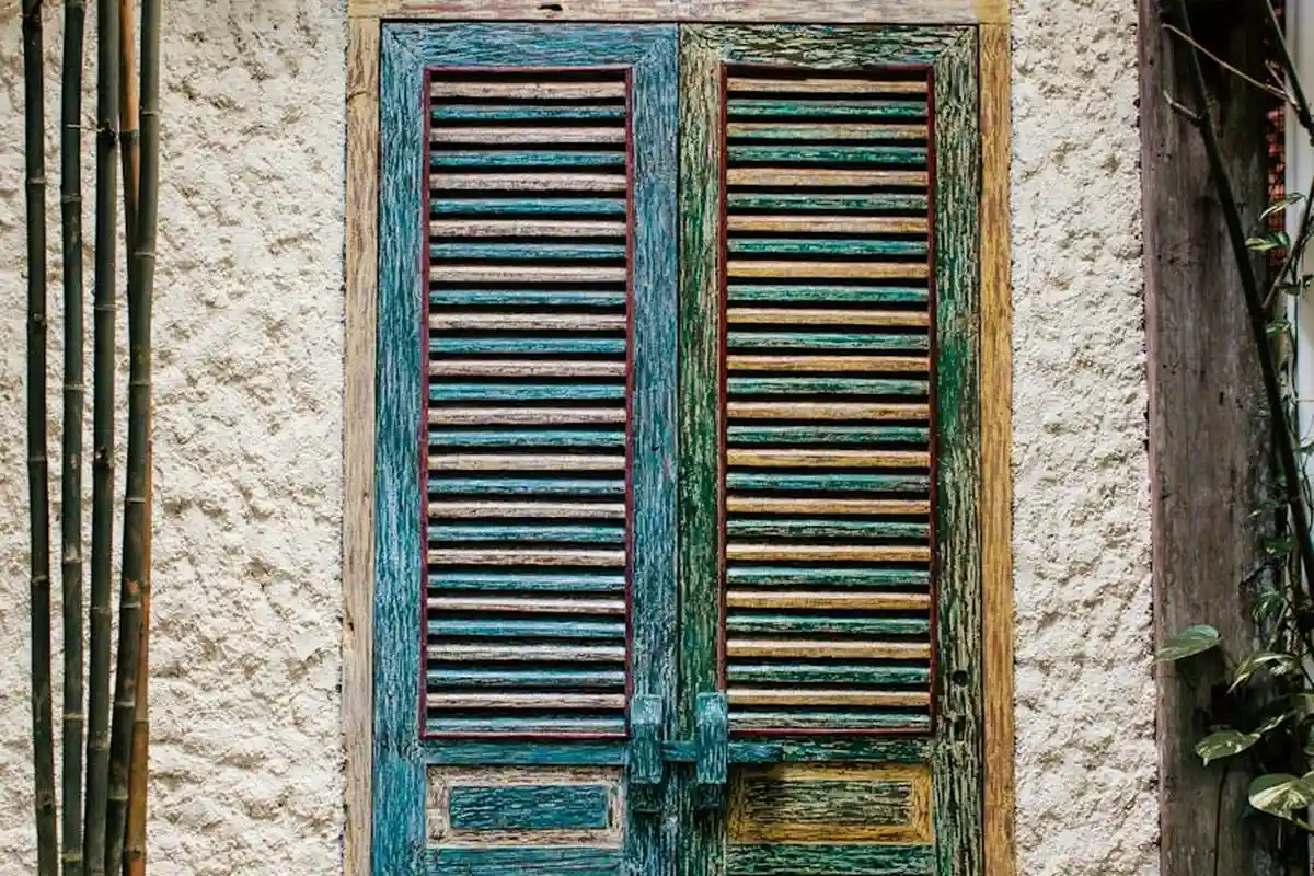 Weathered blue-green wooden door with slatted shutters showing peeling paint and exposed grain.