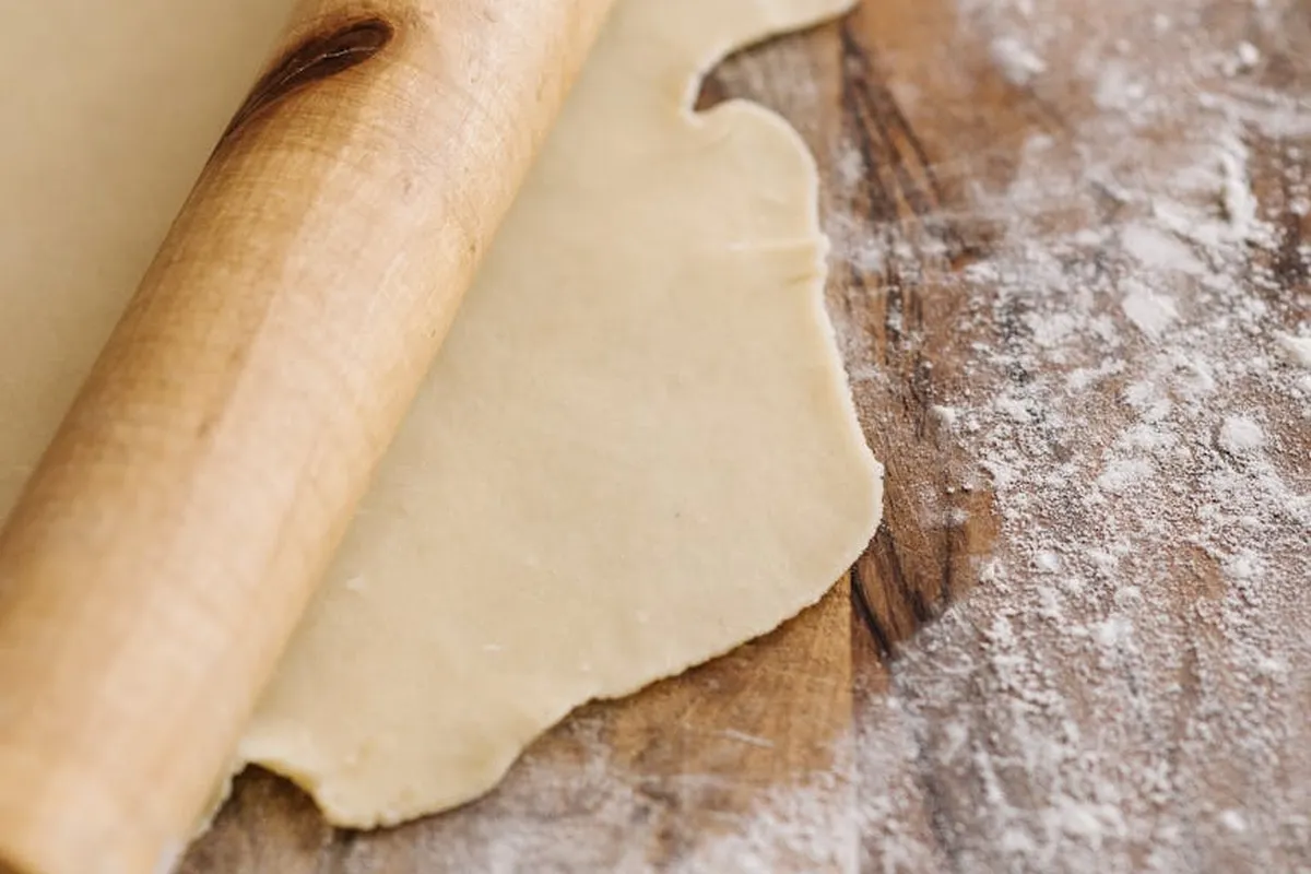 A wooden rolling pin next to a sheet of rolled dough on a flour-dusted wooden surface