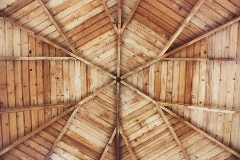 Interior view of a wooden ceiling with radial trusses converging at the center, showing natural wood grain and joinery.