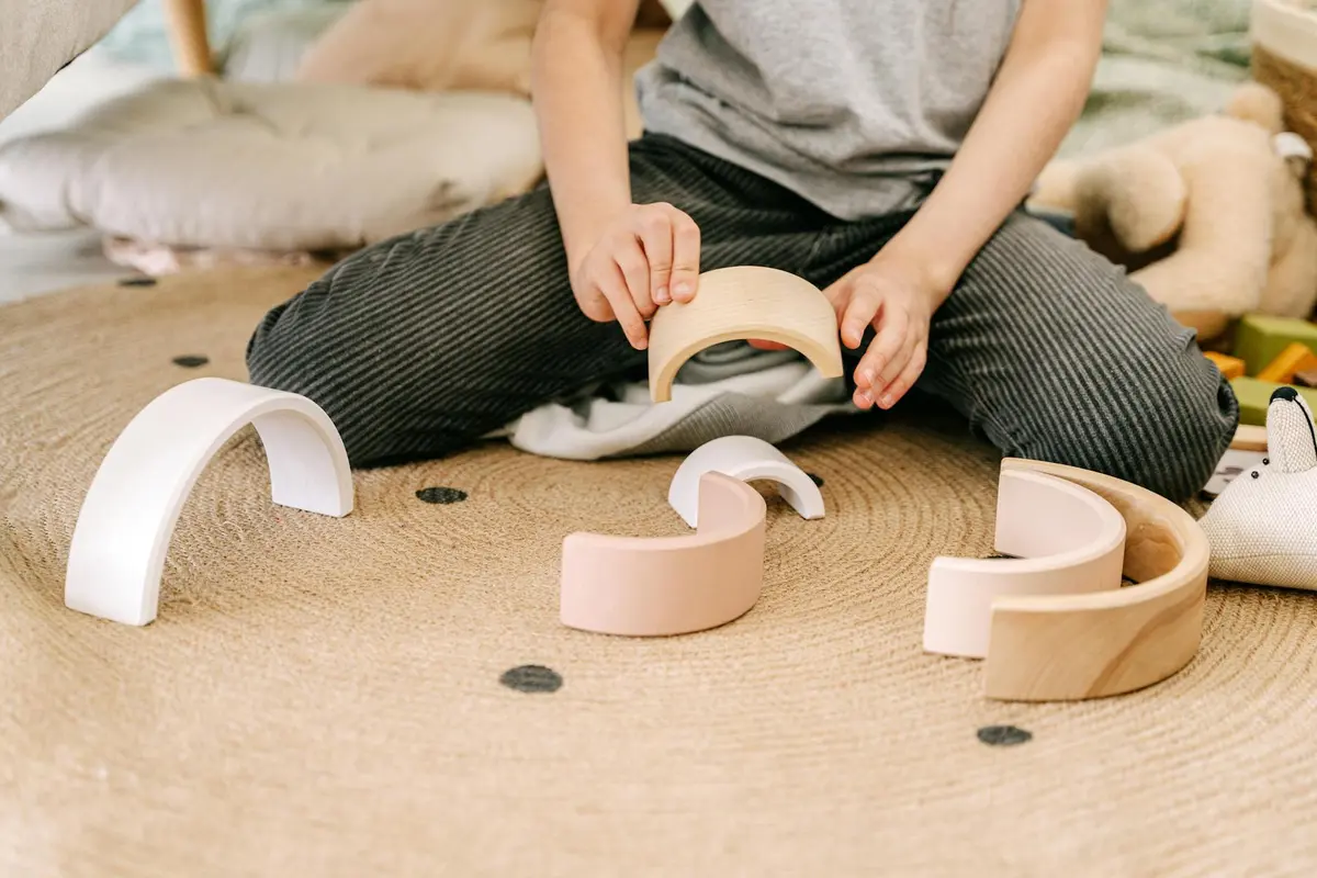 Child seated on a soft rug, playing with curved wooden toy pieces.
