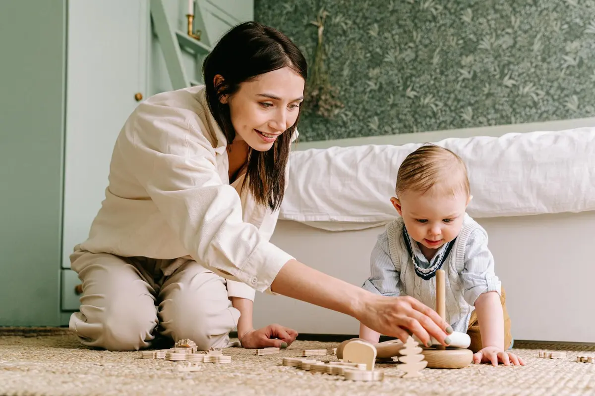 Adult and child playing with wooden stacking toys on a carpet, illustrating durable joinery for active play.