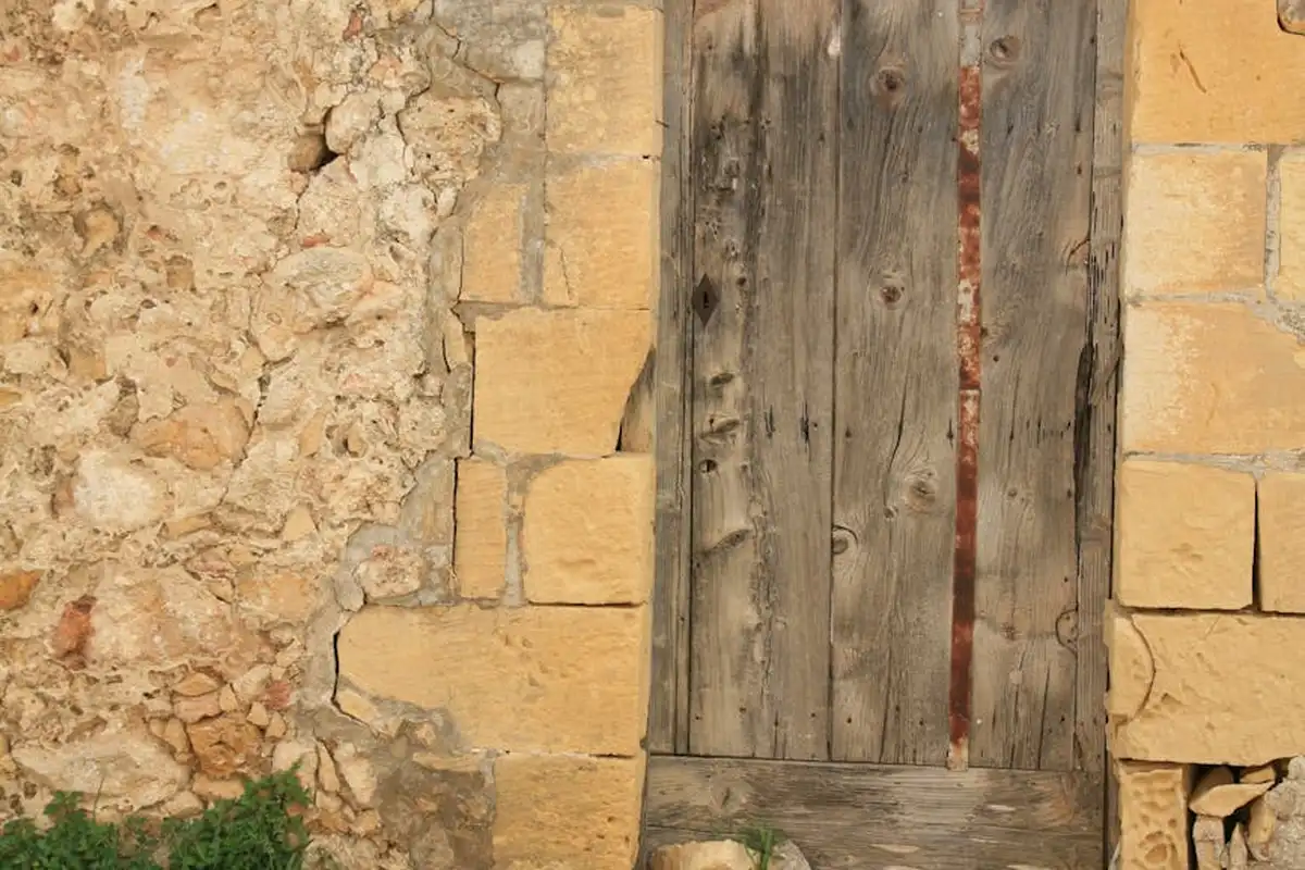Weathered wooden door set in a rough stone wall, showing aging wood and masonry.