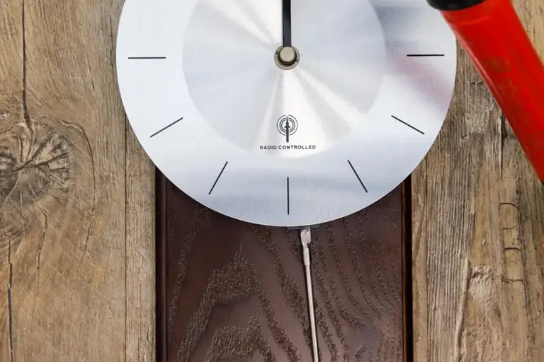 Close-up of a silver circular dial with black marks on weathered wooden planks, with a red tool visible in the top-right corner.
