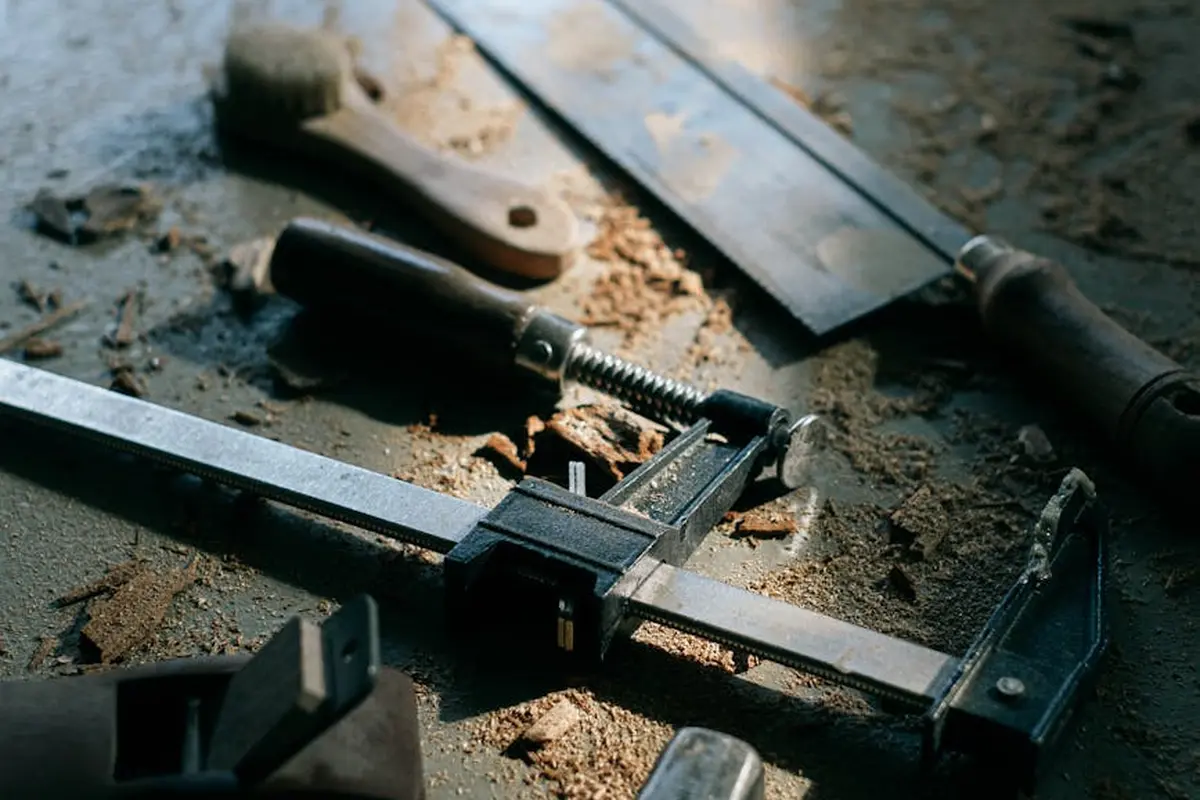 Close-up of a woodworking workbench with sawdust, a caliper, and other hand tools, illustrating a workshop at the limit of a basic dust-control setup.
